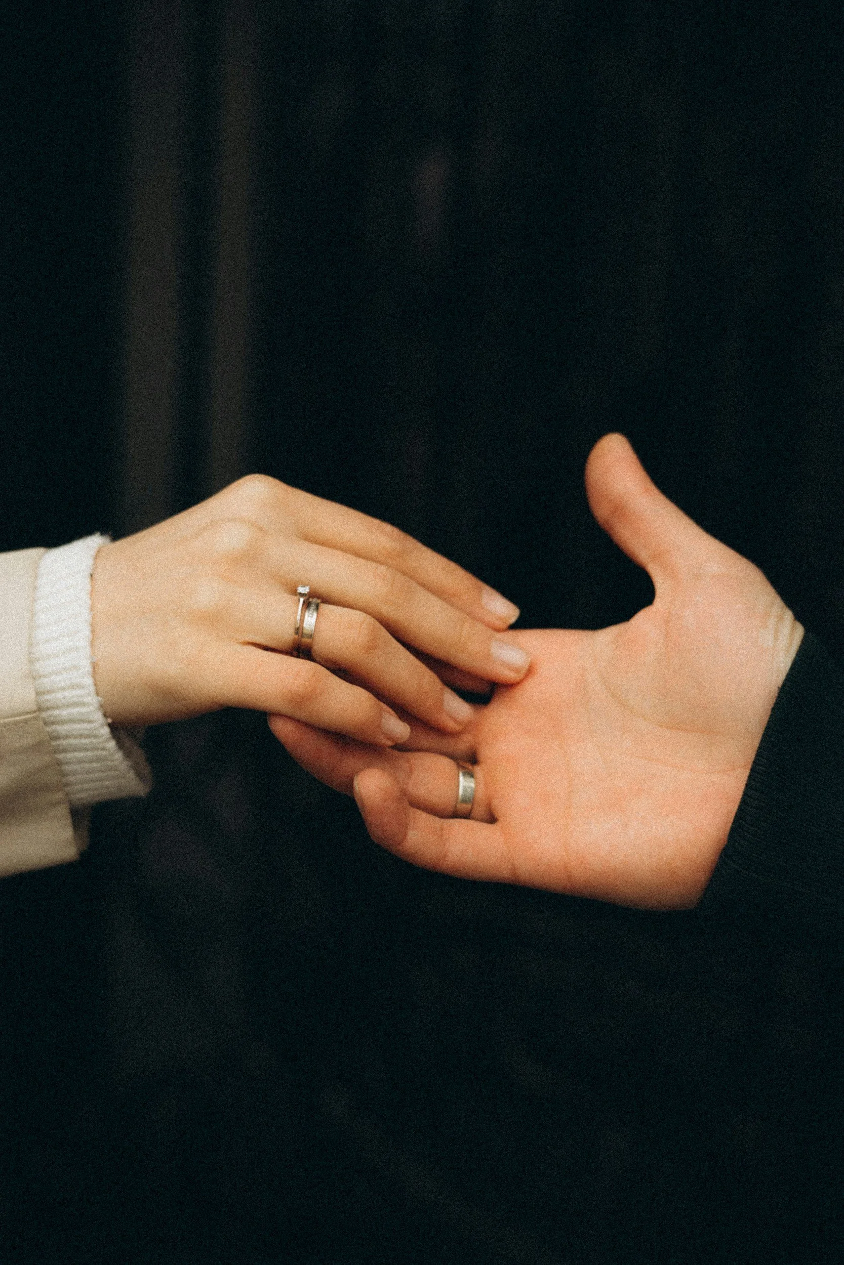 Two hands, one with a ring, gently touching each other against a dark background.