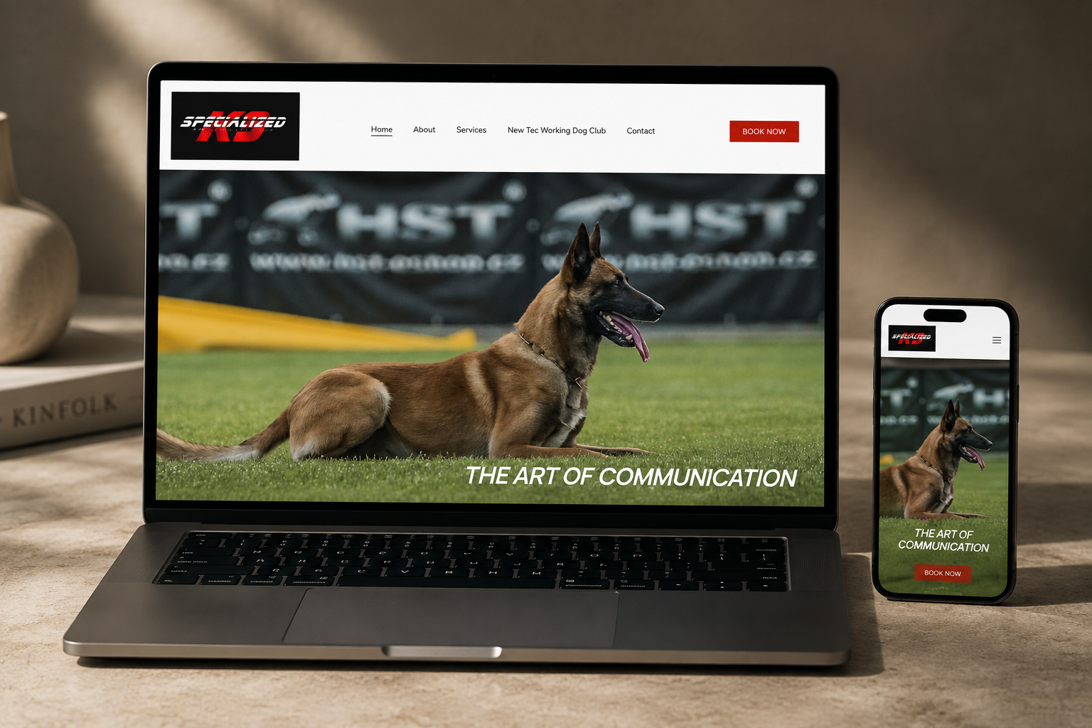 A laptop and smartphone displaying a website featuring a Belgian Malinois dog lying on grass at a training facility with the text "The Art of Communication" and a red "Book Now" button.