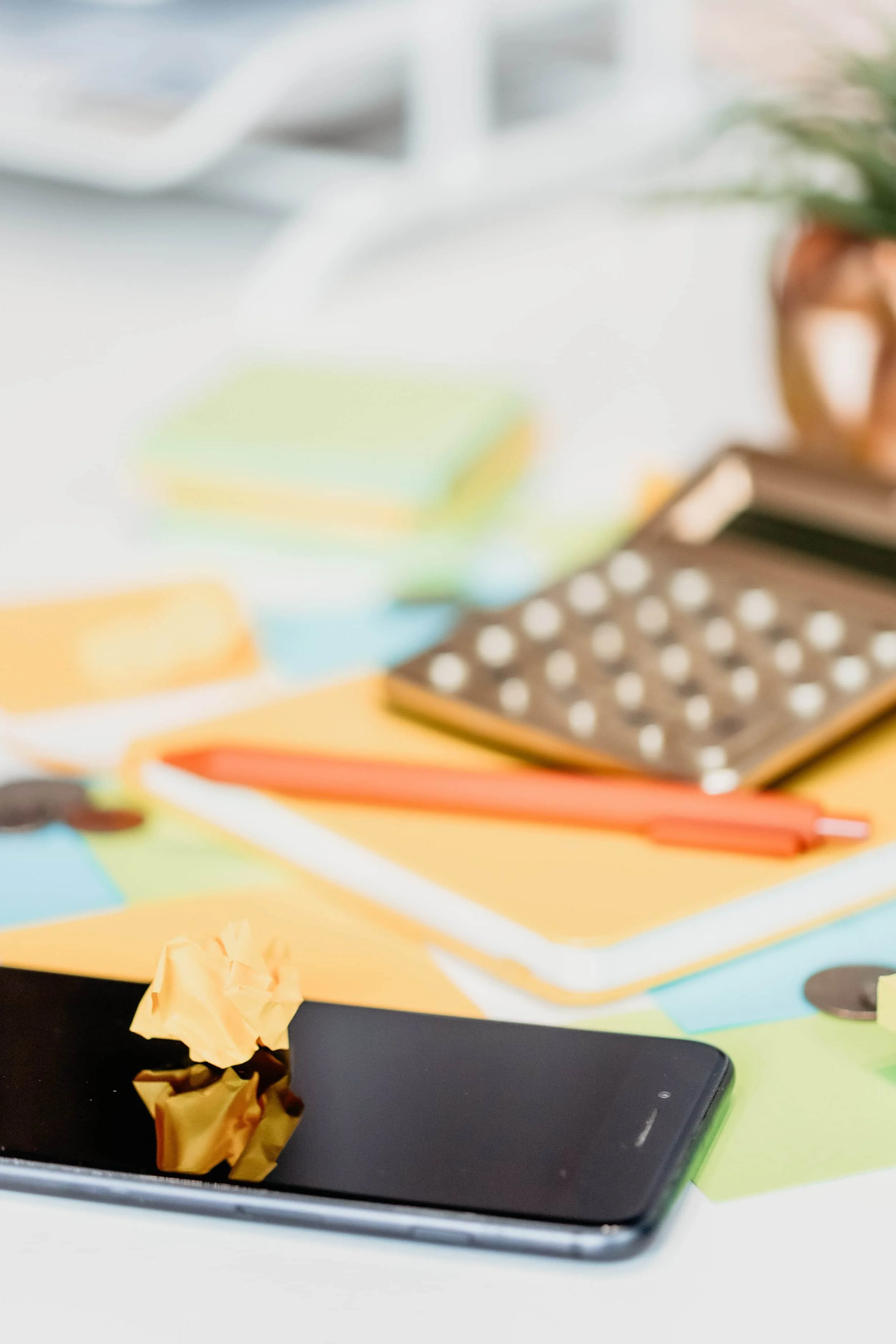 A crumpled yellow paper sits on a smartphone, with a calculator, pen, and notebooks in the blurred background.