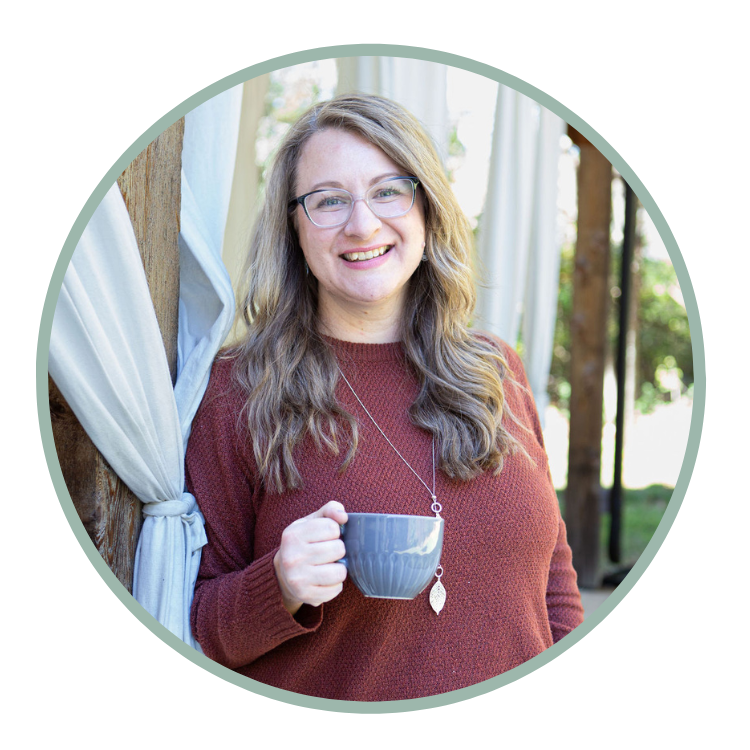 A smiling woman with glasses holding a gray coffee mug outside near a wooden post and curtains, with trees in the background.