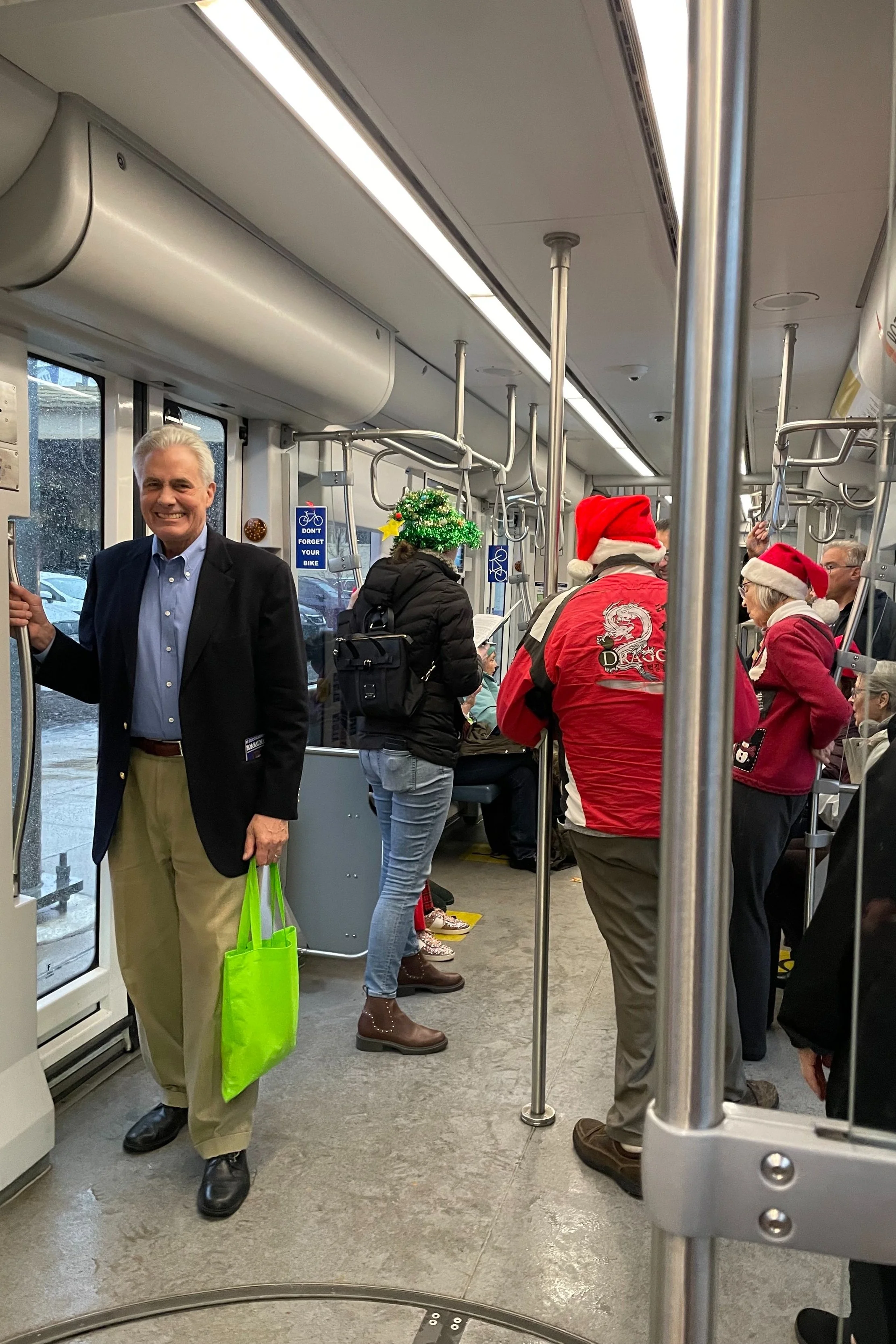 People celebrating Christmas on a bus, some wearing Santa hats and holiday sweaters, with festive decorations like a Christmas tree hat visible.