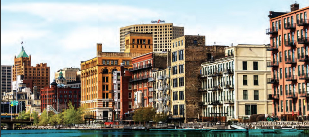 City skyline with colorful historic buildings along a river under a partly cloudy sky.
