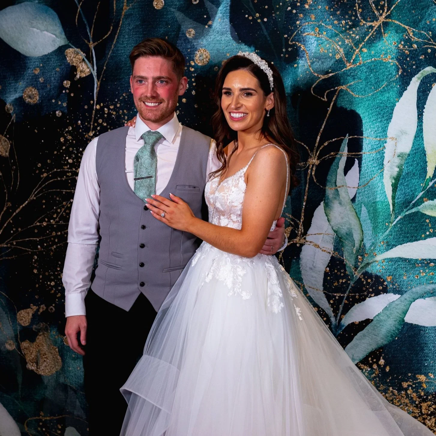 Bride and groom smiling in front of a decorative wall.