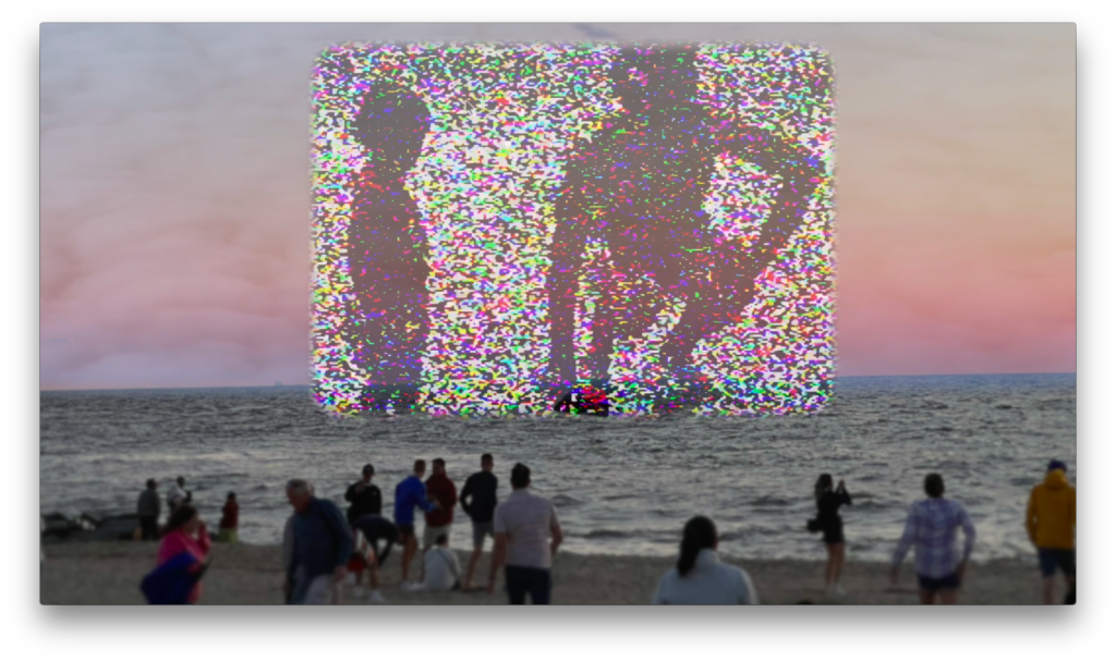 A group of people on a beach watching a large, colorful, glitching digital projection displayed over the ocean water