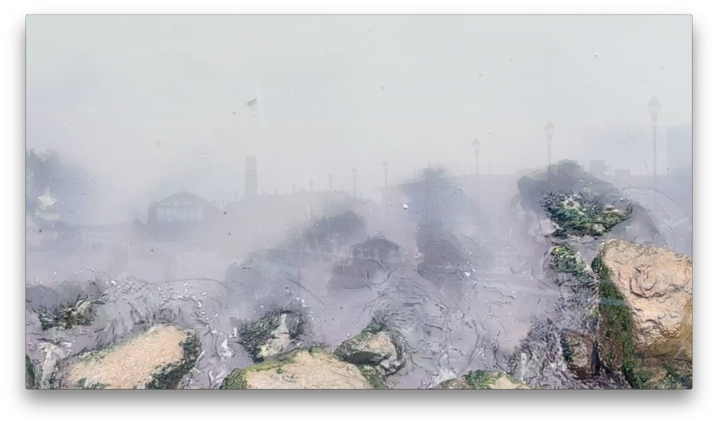 A foggy scene with rocks in the foreground and a faint view of a town or city in the background, including structures like street lamps and a tall tower, obscured by the fog.