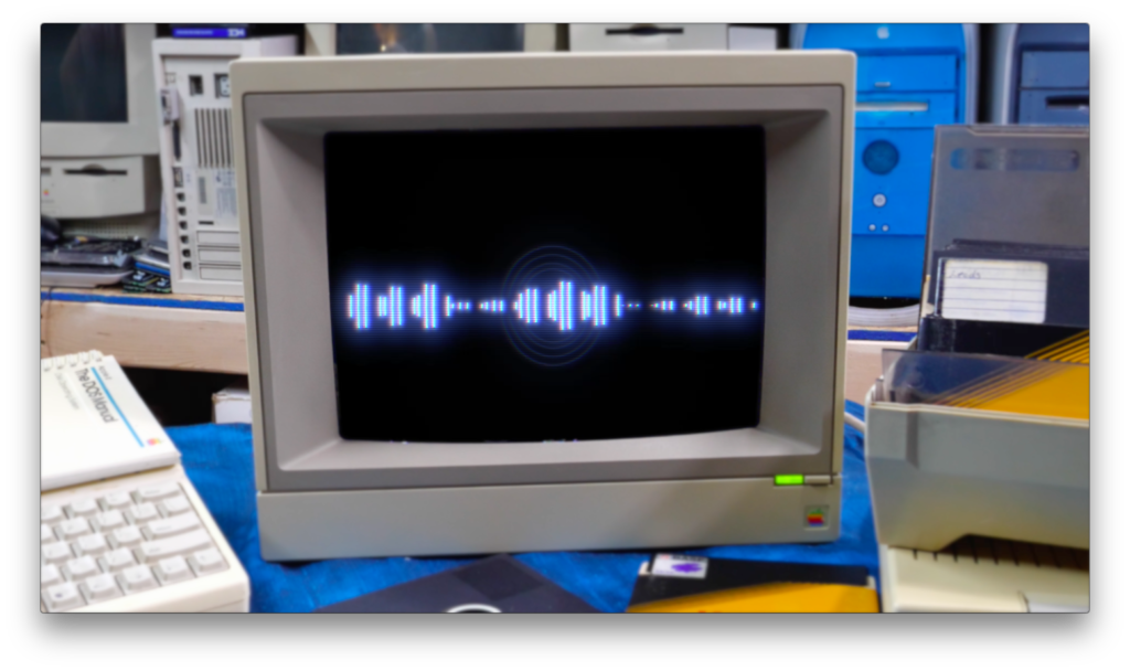 An old computer monitor displaying a blue soundwave pattern on a black background, surrounded by vintage computer equipment and office supplies.