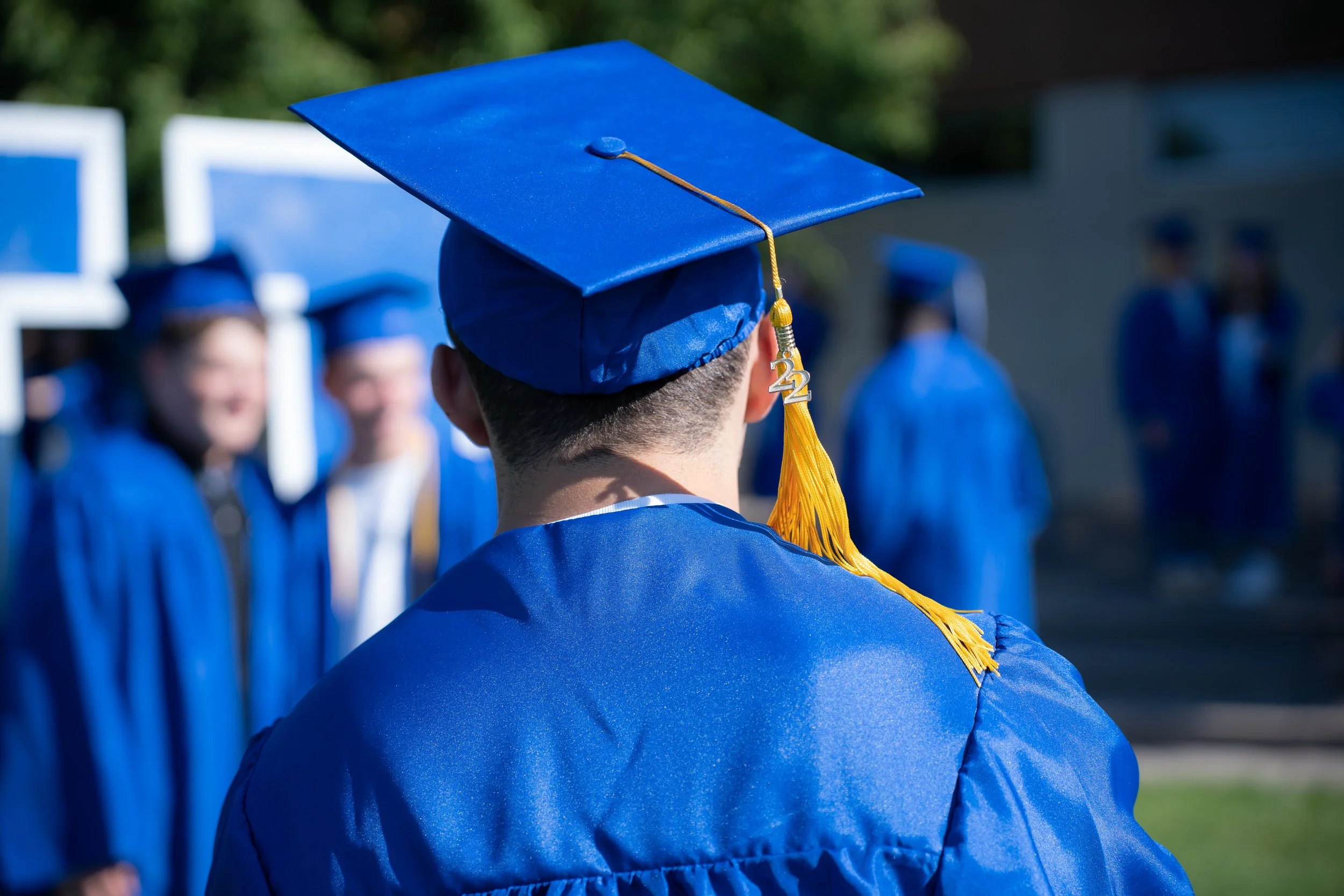 Photograph of the back of a white male high school student's head, wearing royal blue cap and gown