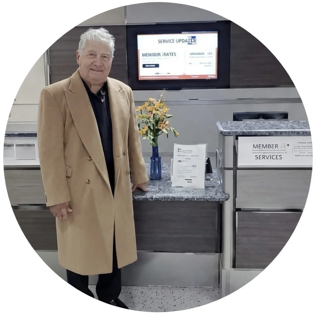 A man in a tan coat standing at a service desk with flowers and informational papers, with a digital screen in the background showing service update information.