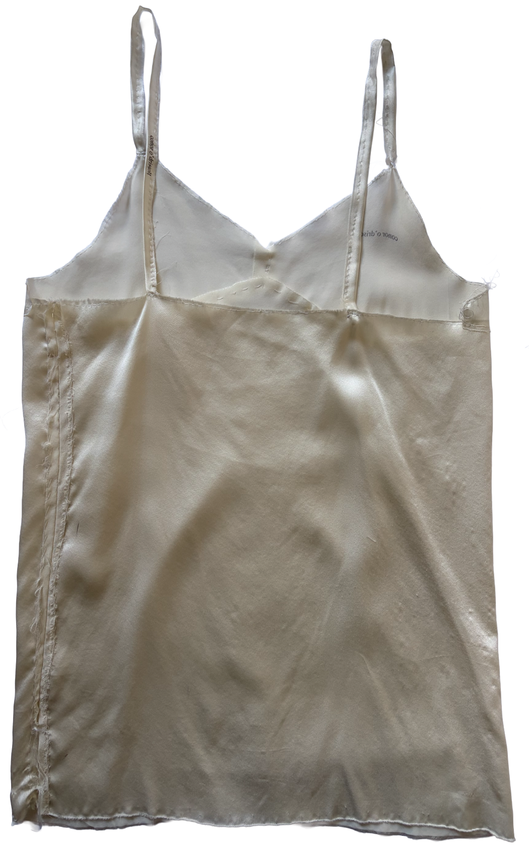 Close-up of a ivory silk slip dress with thin shoulder straps and visible stitching. by conor o'driscoll