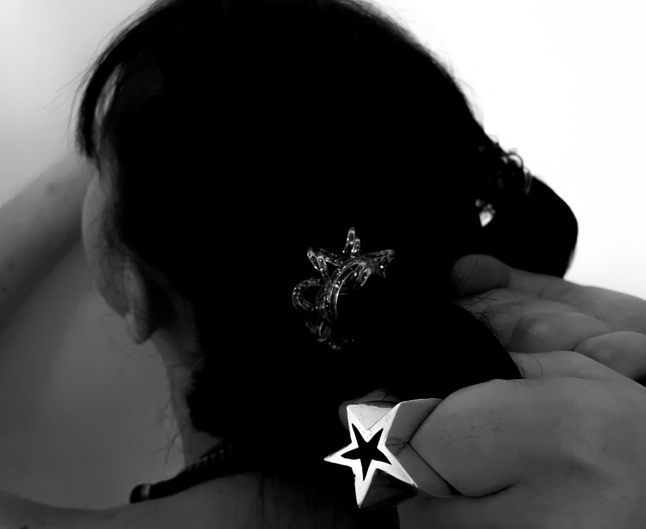 Close-up of a person's head with dark hair, hair clips, and jewelry, resting their hand on their face in black and white photograph. conor o'driscoll