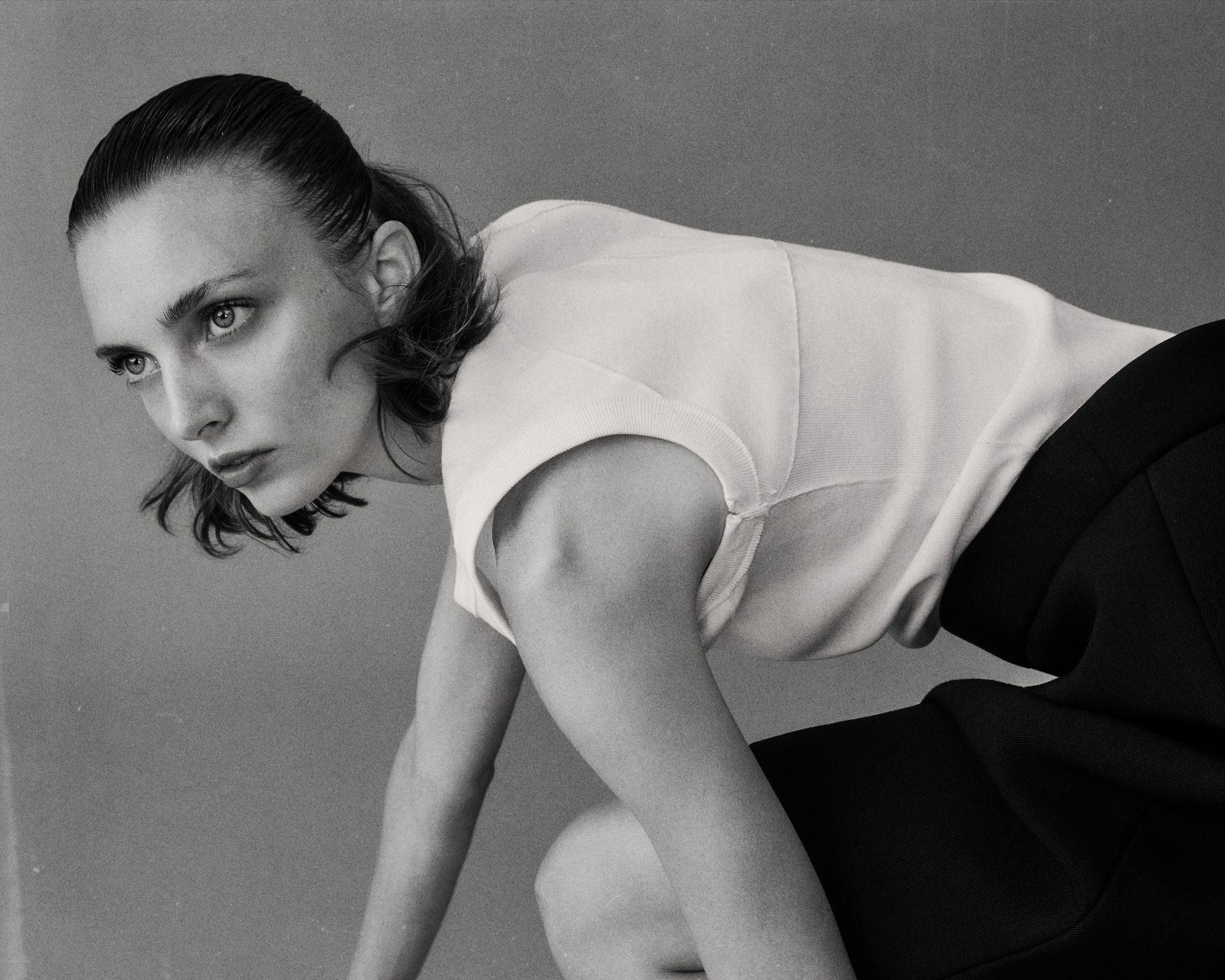 A black and white photograph of a woman with wet hair, lying on her side with her face visible. She is wearing a sleeveless top and looking towards the left. The background is plain and smooth. conor o'driscoll