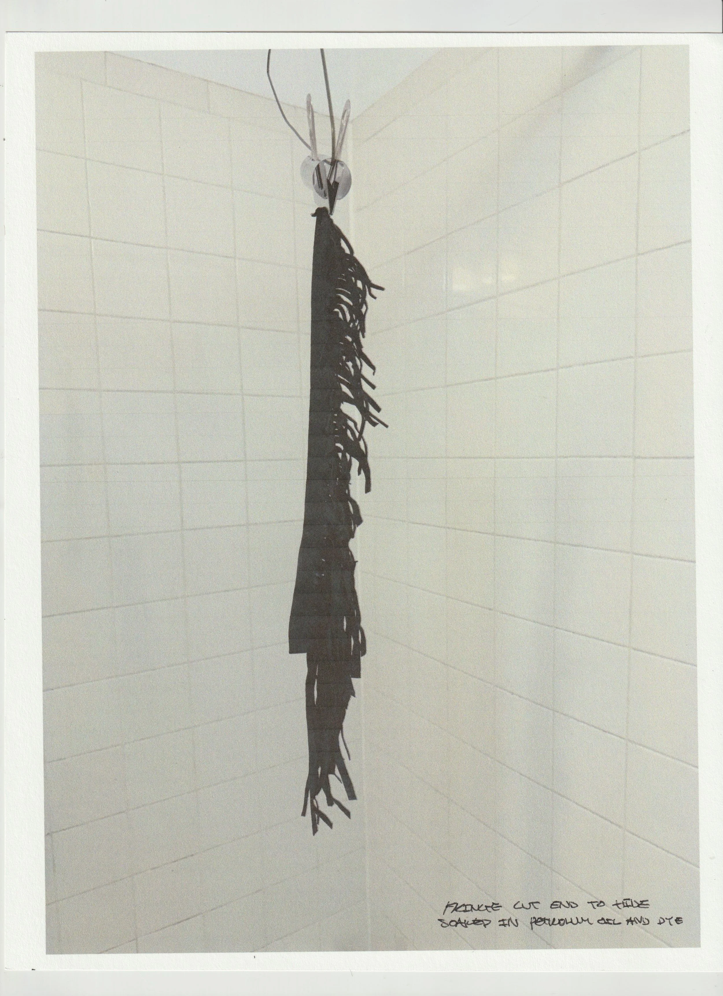 A black frayed piece of fabric hanging from a ceiling hook in a white-tiled room, with handwritten text reading 'Fringe cut end to make skirted in perreaux gel and die' at the bottom right. conor o'driscoll