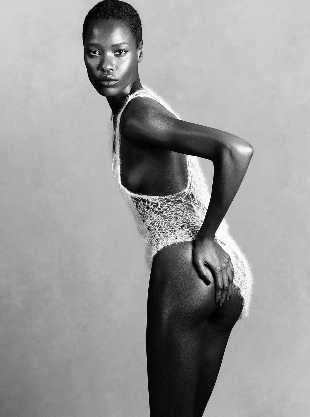 Black and white photo of a woman with short hair, wearing a crochet top, standing with her body turned to the side and her head facing forward. conor o'driscoll LUIGI AND IANGO