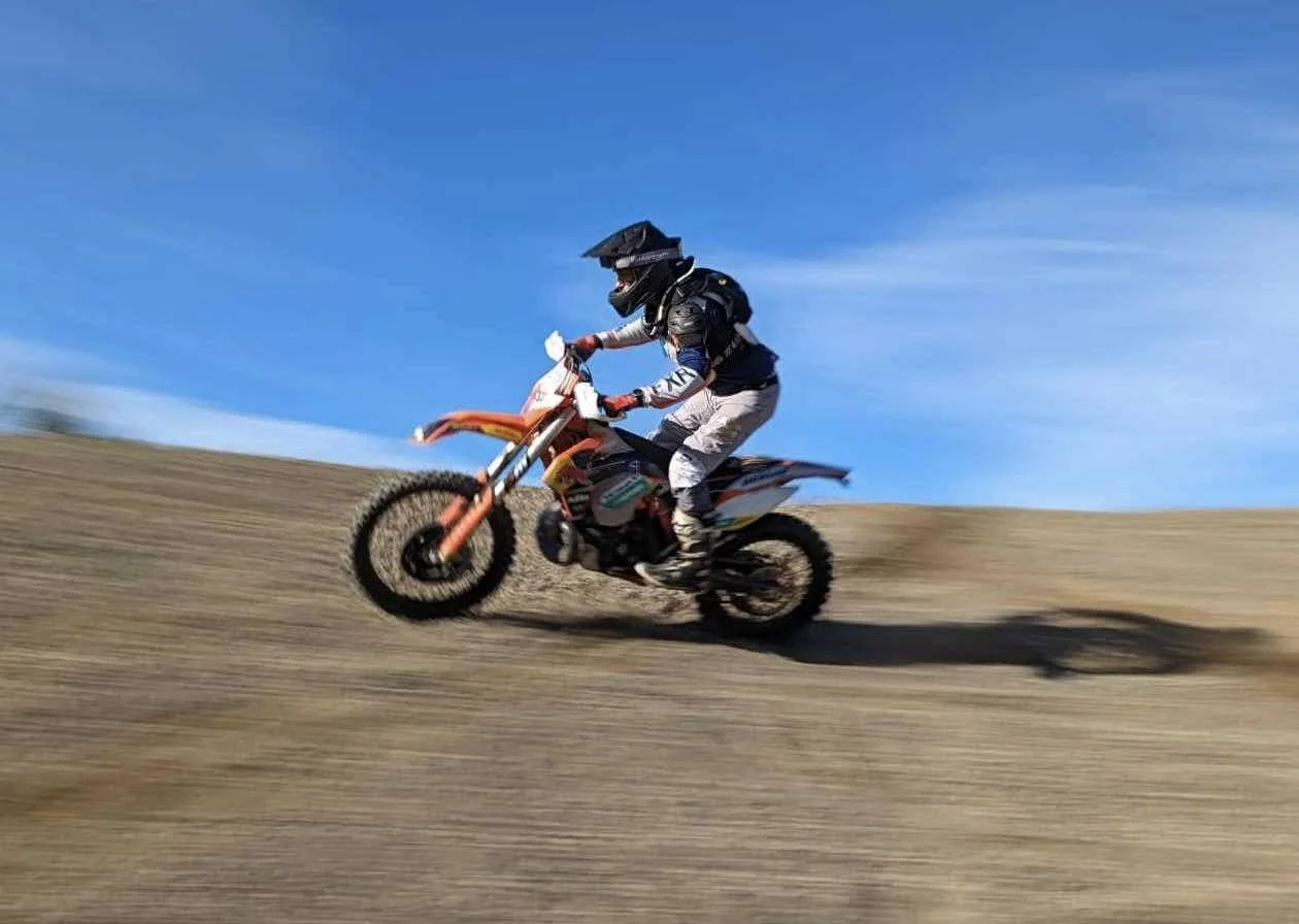 Motorcyclist riding dirt bike on dirt trail under blue sky.