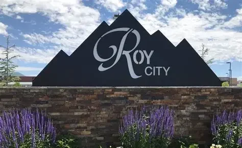 Roy Utah city sign with blooming purple and green flowers at the base, near residential and commercial areas served by asphalt paving, repair, and maintenance services.