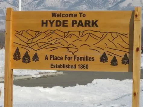 Wooden Hyde Park Utah city sign reading ‘A place for families, established in 1860’ with snow on the ground, near residential and commercial areas served by asphalt paving, repair, and maintenance services.
