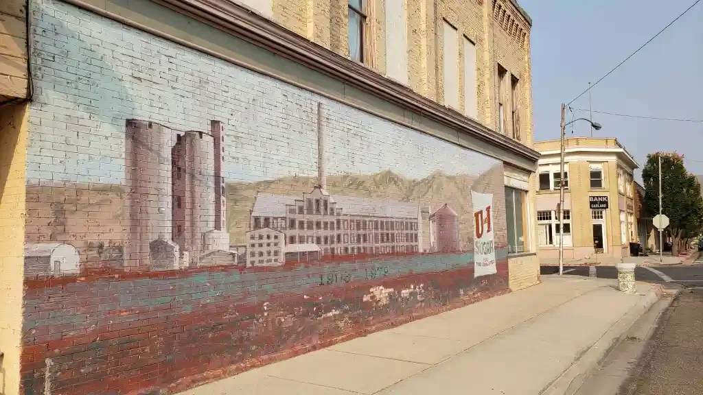 Downtown Garland Utah brick building with a painted mural of the historic sugar factory, near residential and commercial areas served by asphalt paving, repair, and maintenance services.