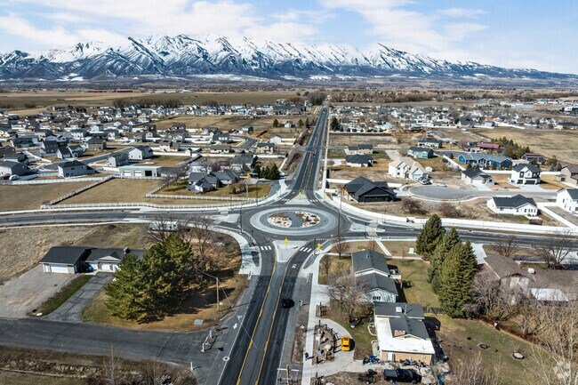 Large roundabout on 2600 South in Nibley Utah looking west toward distant snow‑covered mountains, near residential and commercial areas served by asphalt paving, repair, and maintenance services.
