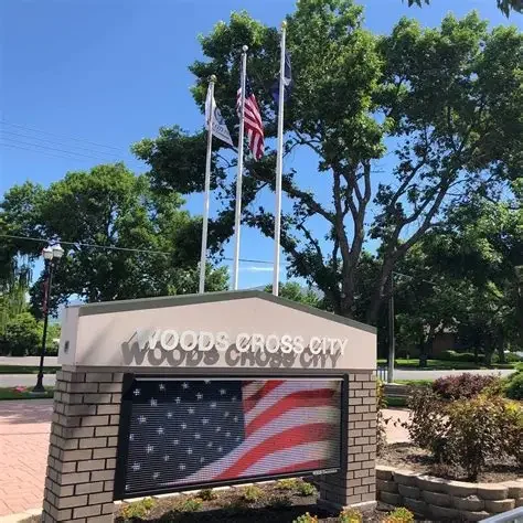 Woods Cross Utah City Hall sign with three flags and green trees overhead, serving nearby residential and commercial areas with asphalt paving, repair, and maintenance services.