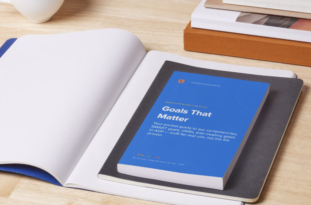 A book titled "Goals That Matter" placed on top of an open notebook on a wooden desk. There are stacked books and a cup in the background.