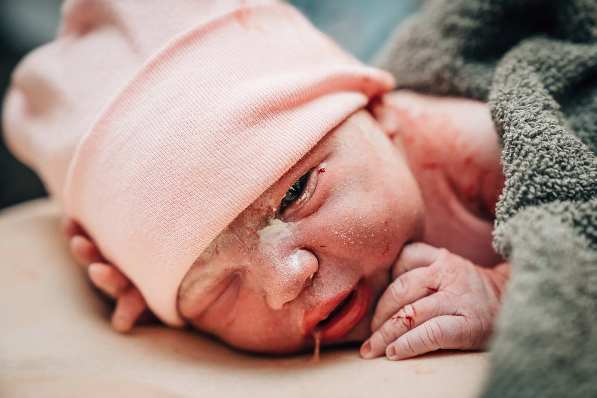 A newborn baby in a pink hat lies skin to skin on their parent's chest shortly after birth. 