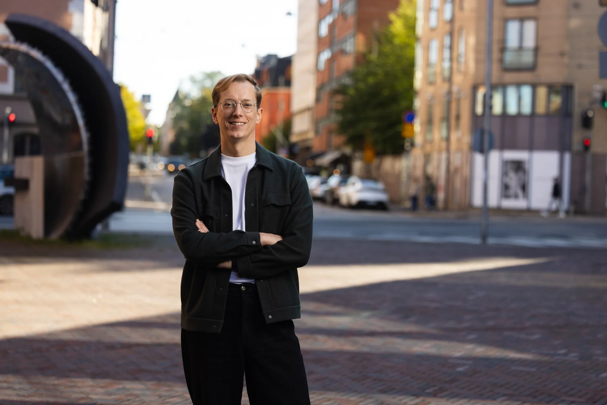 Kuvassa vihreä poliitikko Matti Lehto seisoo ulkona vihreässä takissa ja valkoisessa paidassa, hymyillen kameralle. Taustalla näkyy aurinkoinen Tehtaankatu. Matti Lehto on vihreä eduskuntavaaliehdokas Helsingissä vuoden 2027 eduskuntavaaleissa.