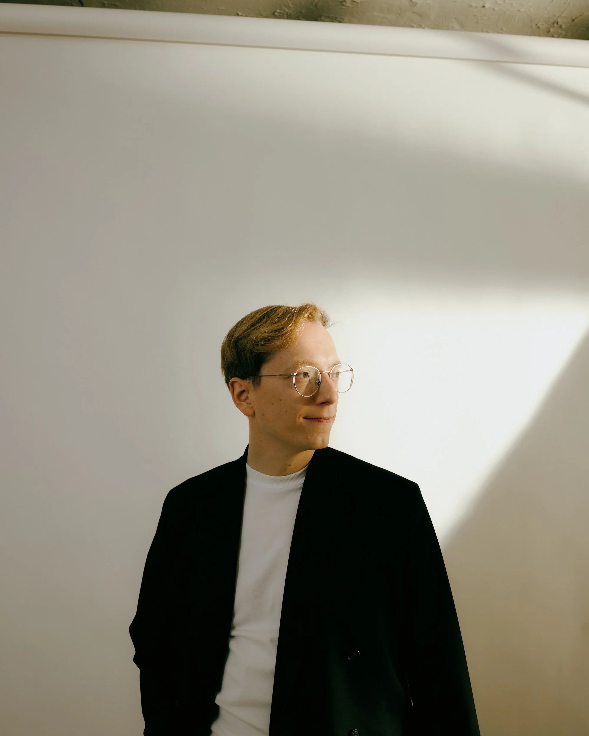 Vihreä poliitikko Matti Lehto, jolla on vaalea tukka ja silmälasit, katsoo oikealle ja seisoo valkoisella taustalla.