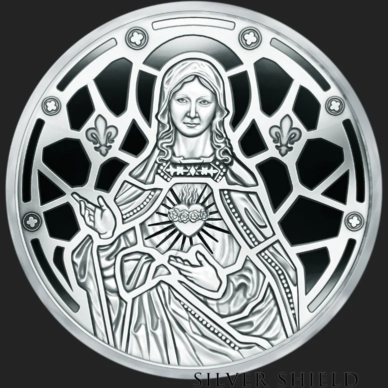 A minted silver proof coin with a depiction of Jesus Christ with a halo, pointing with one hand and holding his heart with the other, surrounded by decorative patterns and small fleurs-de-lis.
