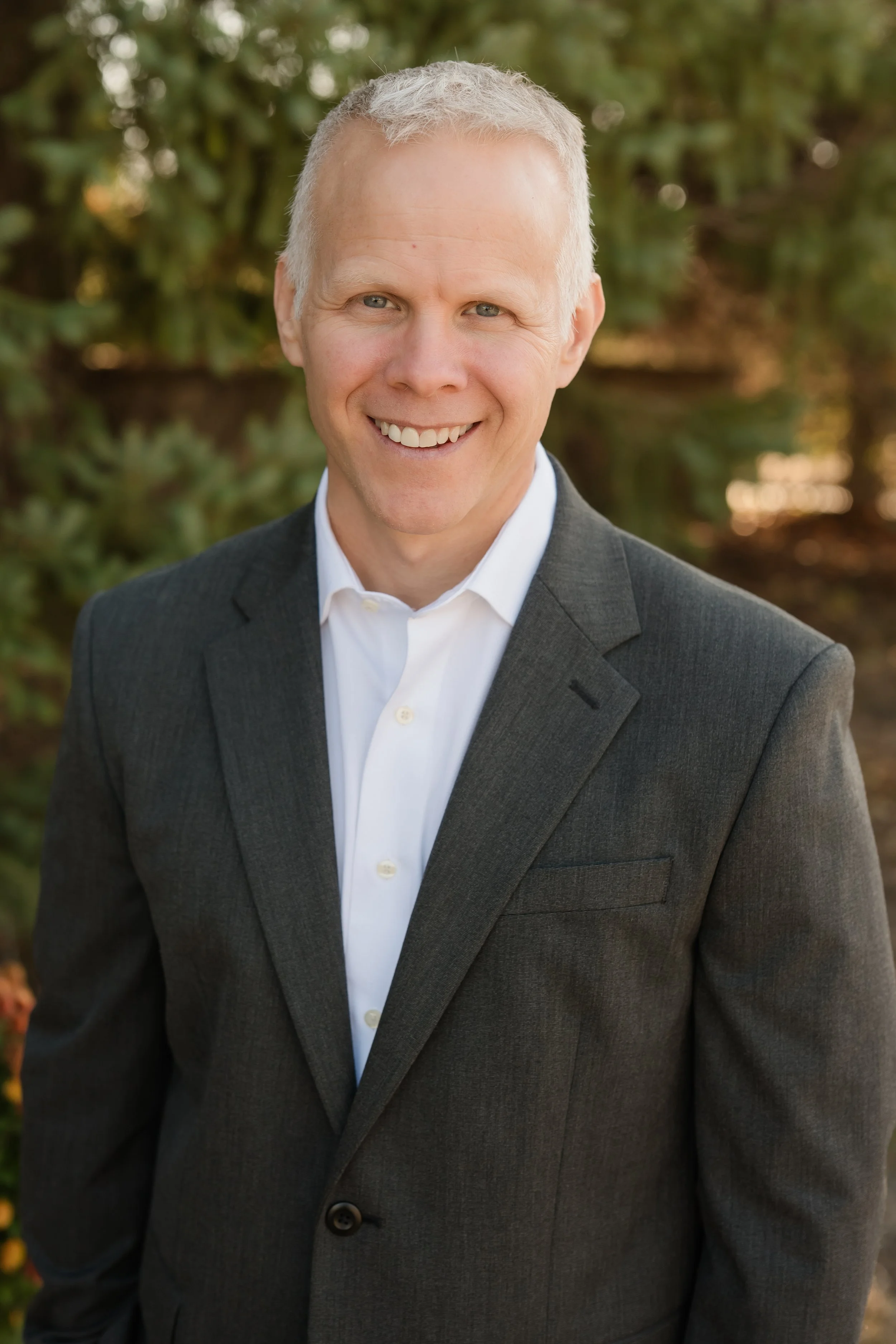 Four people standing outdoors, smiling, in front of lush green plants and trees, under a canopy.