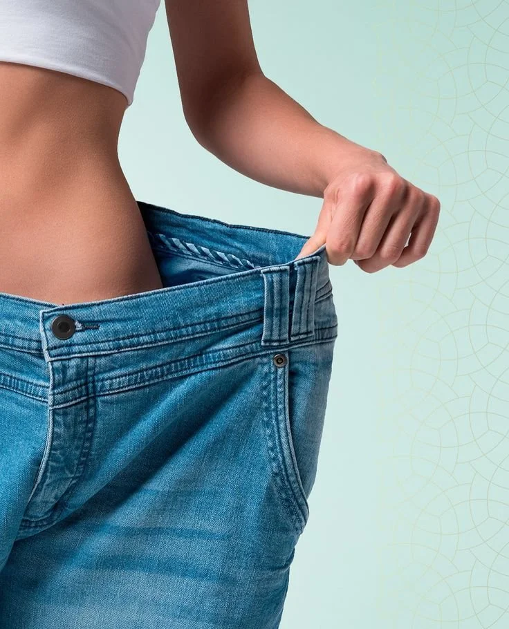 Close-up of a person pinching the waistband of oversized blue jeans, showing they are too big for them.