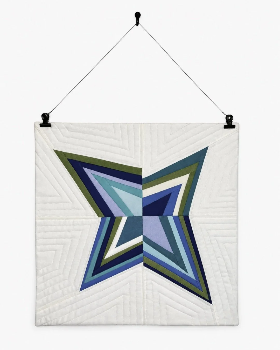 Finished blue, green, and white star mini quilt hanging from two clips and a thin wire