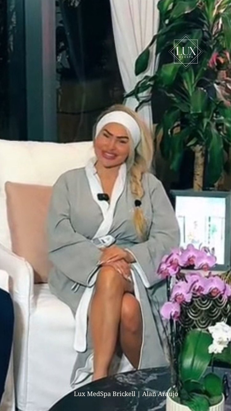 Darcey Silva seated in a spa robe at LUX MedSpa Brickell, beside pink orchids.
