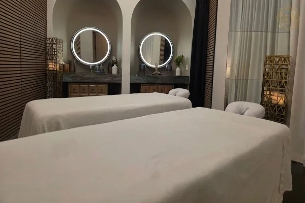 Two side-by-side massage tables with white linens and illuminated round mirrors at LUX MedSpa Brickell.