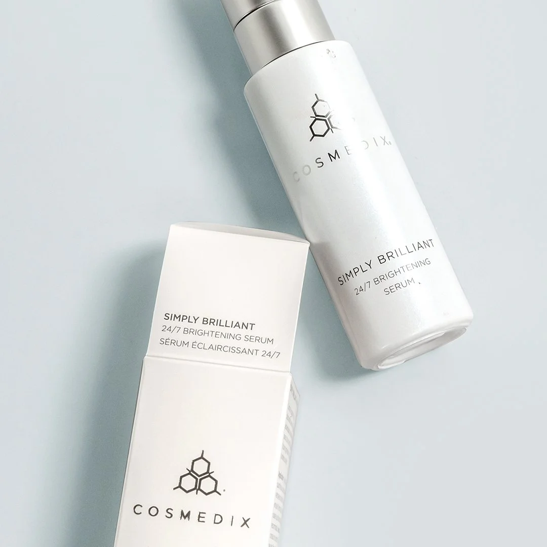 Overhead view of COSMEDIX Simply Brilliant serum and its box arranged diagonally on a pale blue surface.