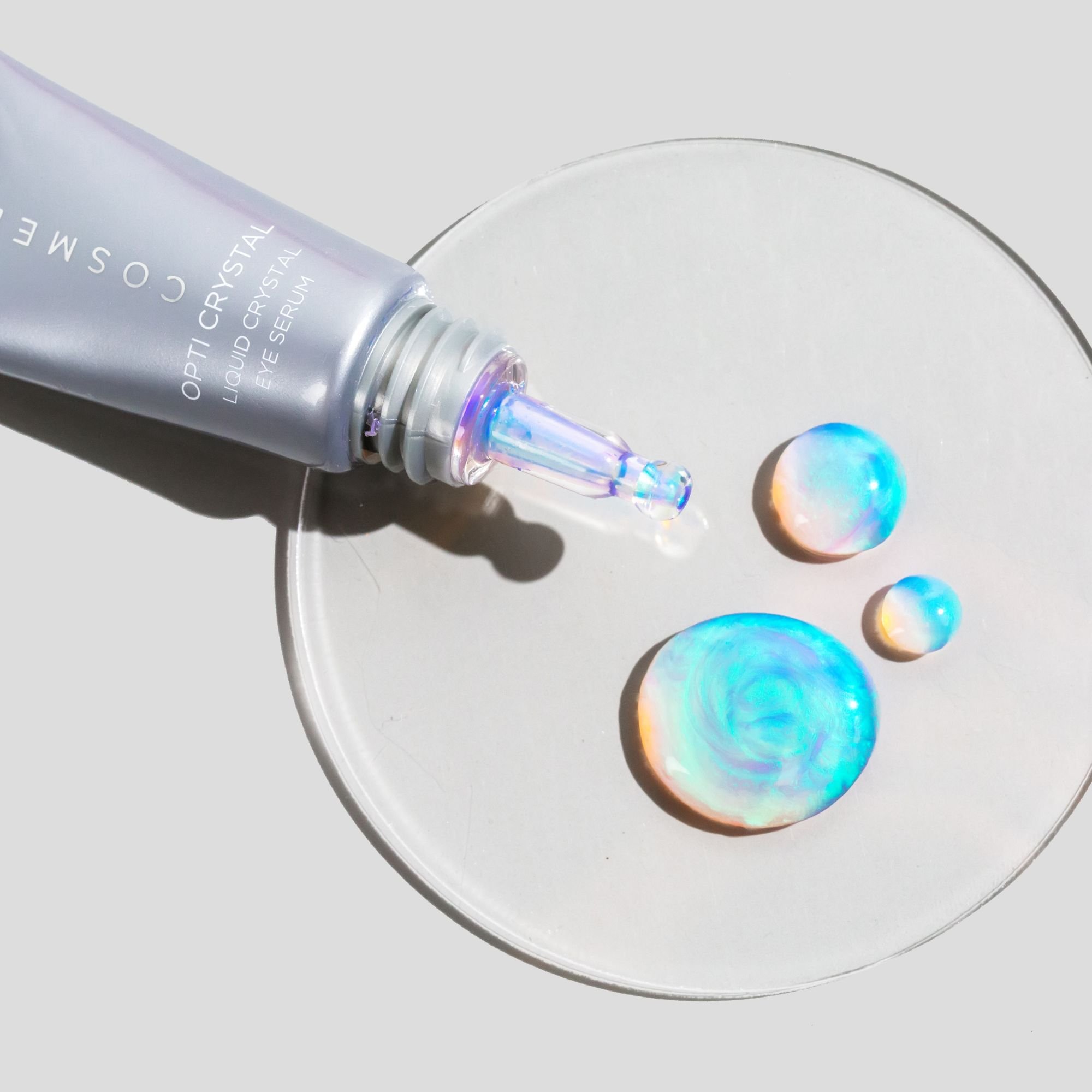 Close-up of the iridescent Opti Crystal eye serum texture beside its tube.