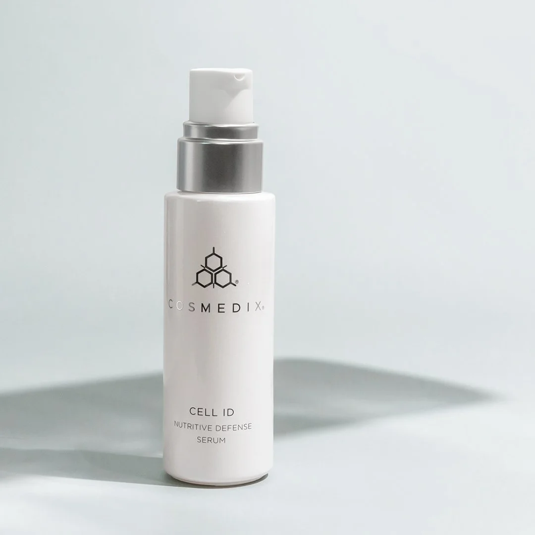 COSMEDIX Cell ID Nutritive Defense Serum pump bottle standing on a pale blue background with soft shadows.