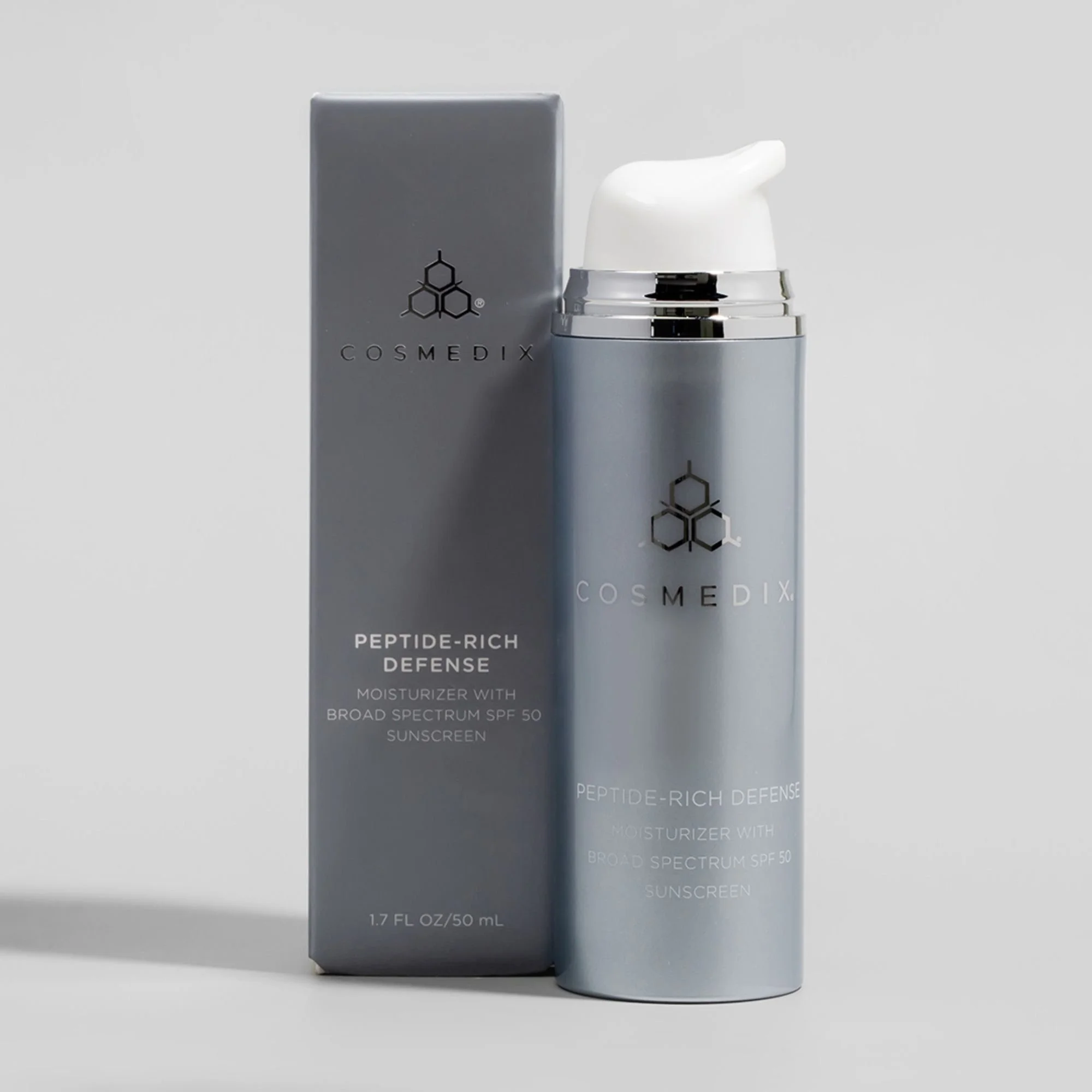 COSMEDIX Peptide-Rich Defense SPF 50 moisturizer bottle displayed next to its elegant, dark grey retail box.