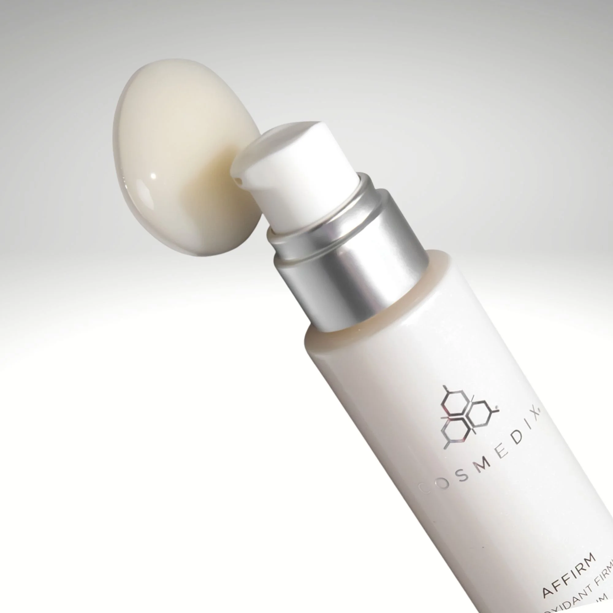 Angled close-up of the COSMEDIX Affirm bottle and pump beside a drop of serum.