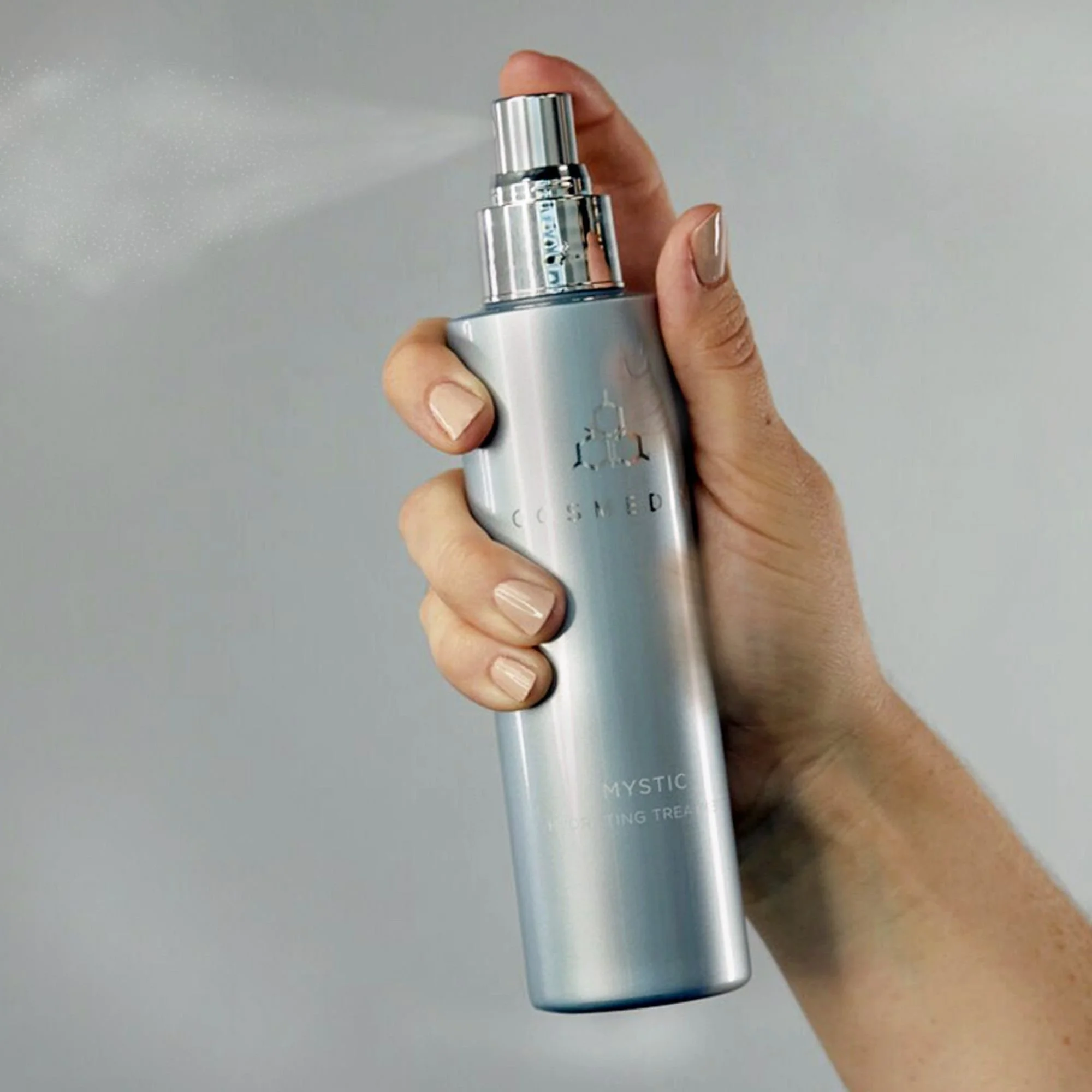 Hand spraying a fine mist from a COSMEDIX Mystic Hydrating Treatment bottle.