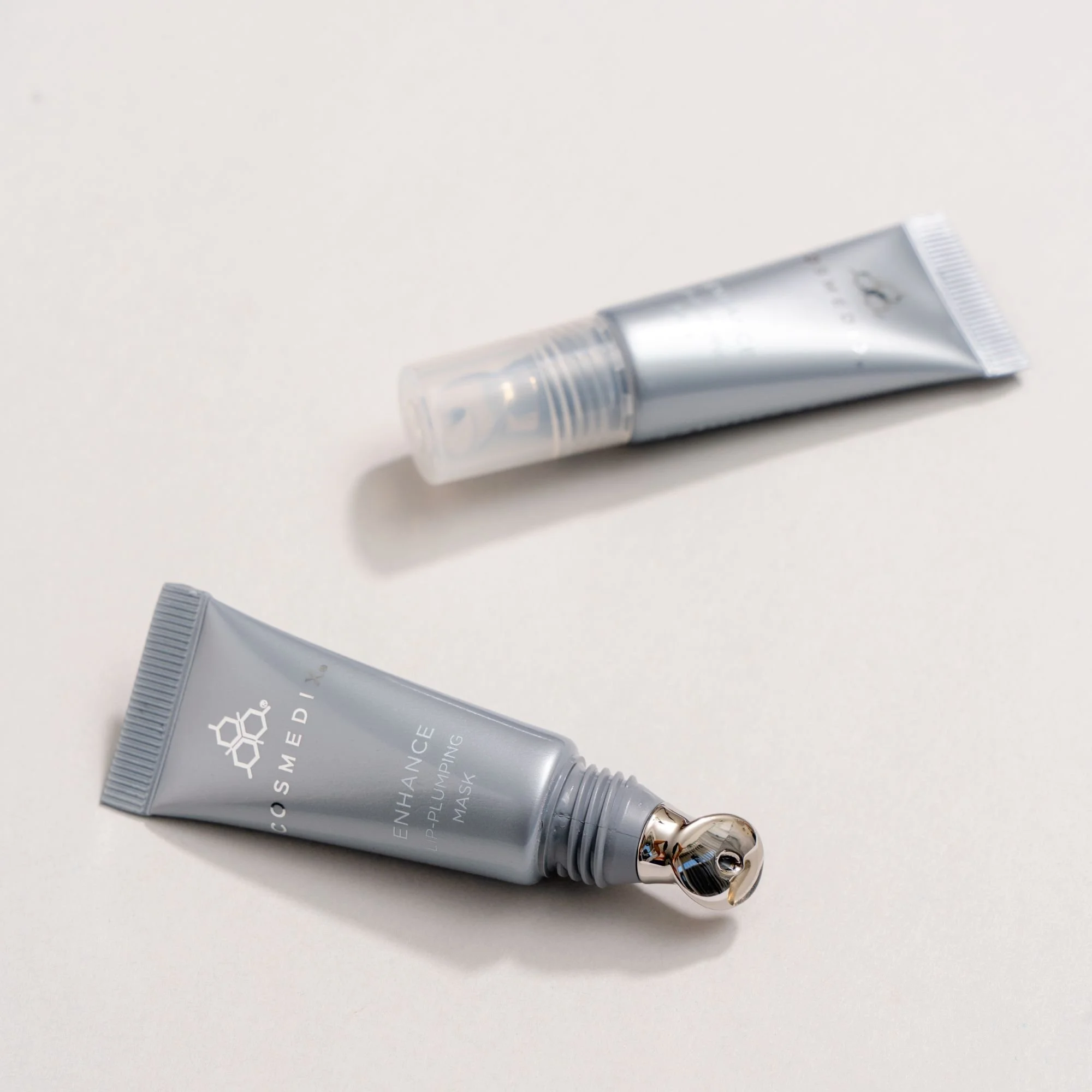 Close-up product photograph of COSMEDIX Enhance Lip-Plumping Mask showing its silver tube and applicator.
