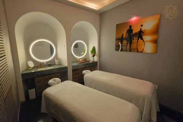 A couples treatment room at LUX MedSpa Brickell, with two massage tables, round mirrors and sunset artwork.