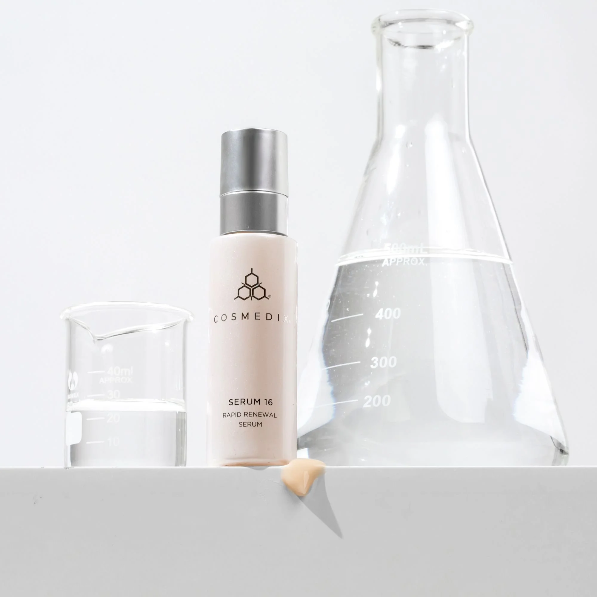COSMEDIX Serum 16 bottle on a white ledge with a serum swatch, glass beaker, and flask