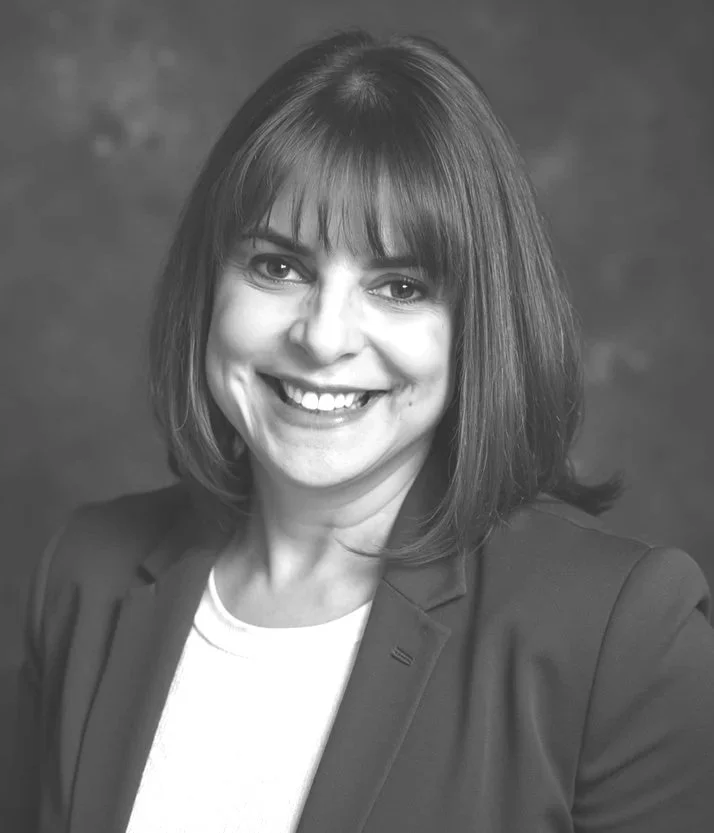 Black and white portrait of a woman with medium-length hair, smiling, wearing a blazer and a light-colored shirt.