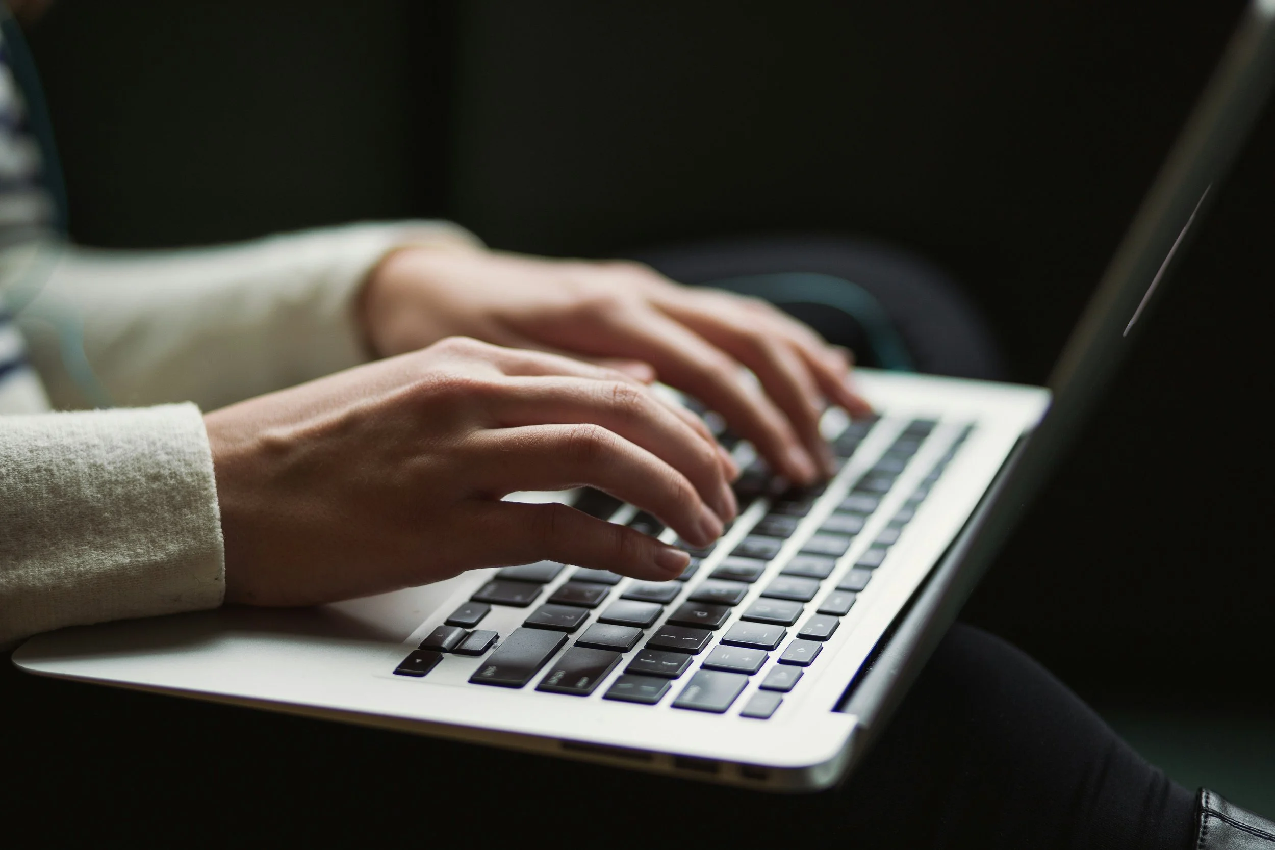 Close-up of hands typing on a laptop keyboard in a dark setting.