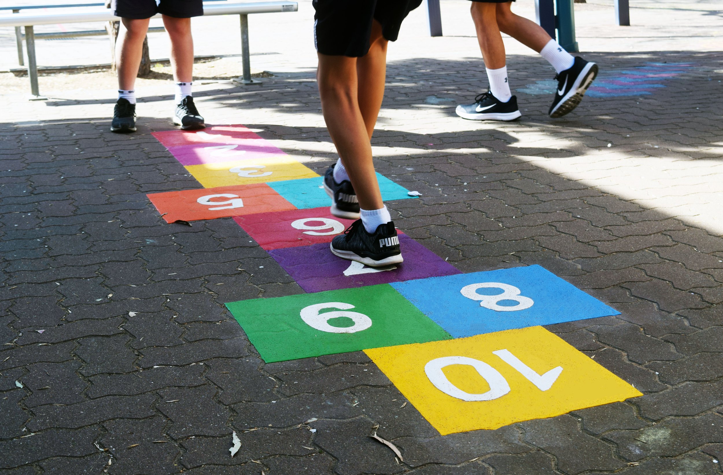 Children playing hopscotch on a colorful numbered grid painted on the ground.