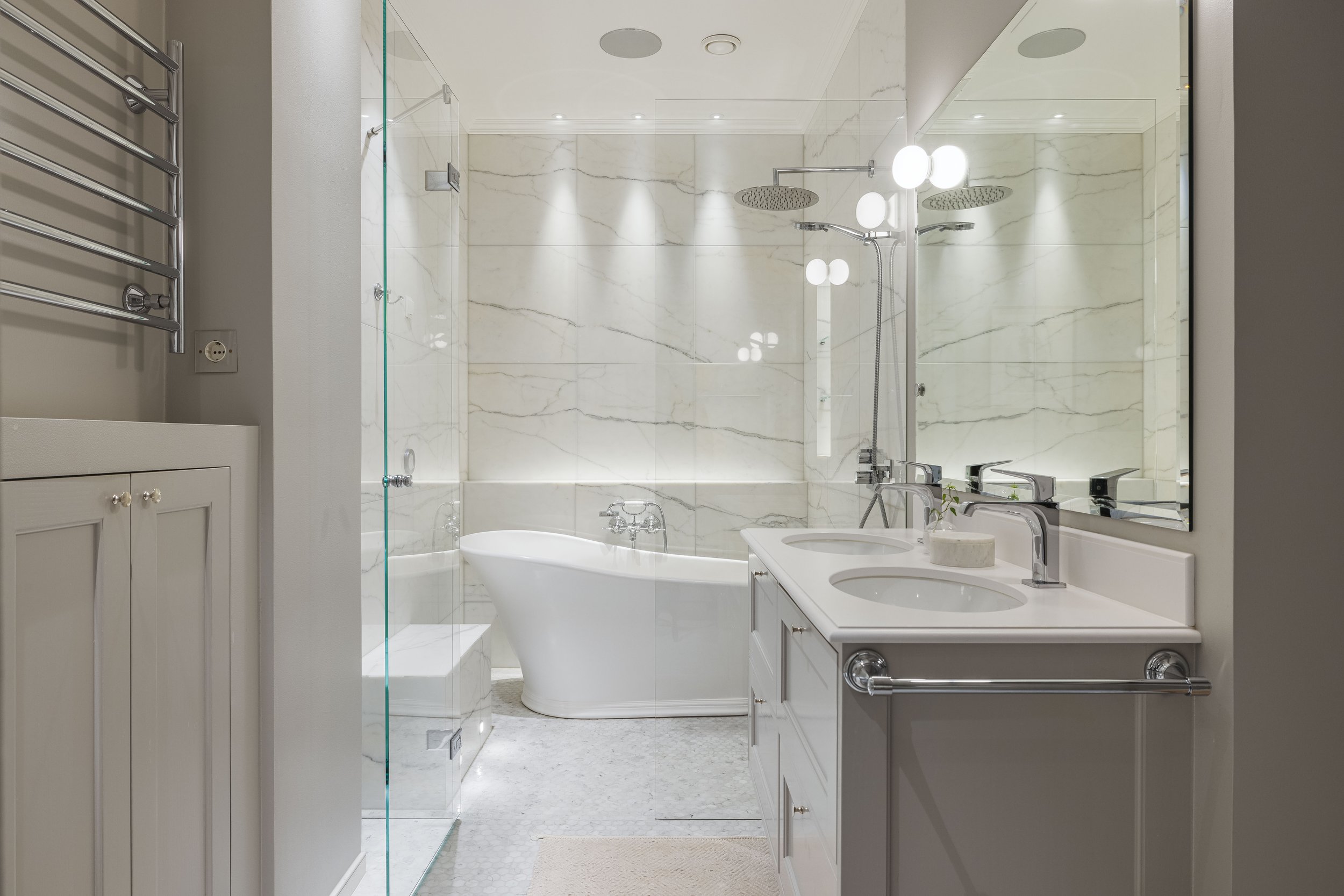 Modern bathroom with freestanding bathtub, glass shower enclosure, dual sinks, and marble tiles.
