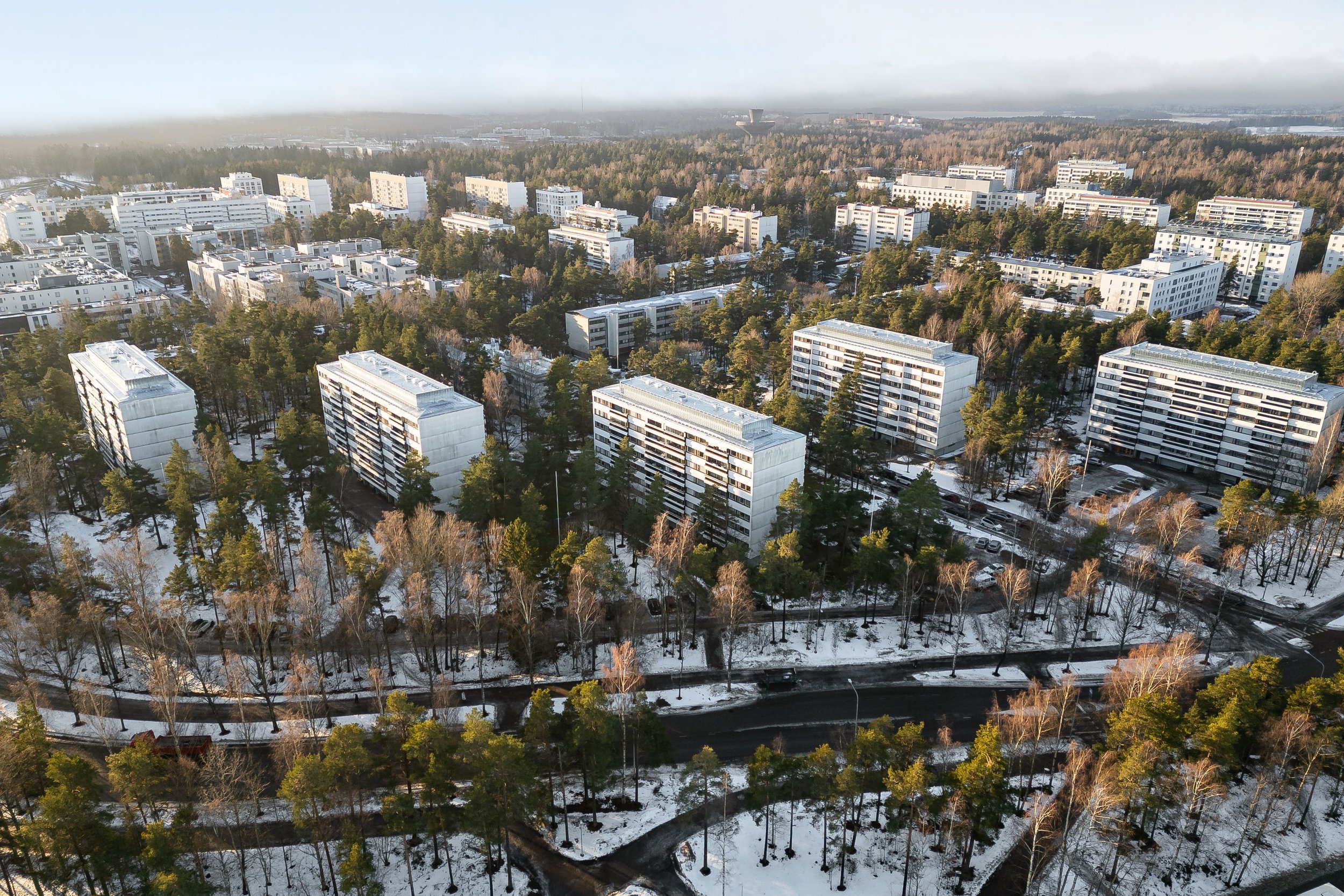 Aerial view of a residential area with multiple apartment buildings surrounded by trees and snow-covered ground.