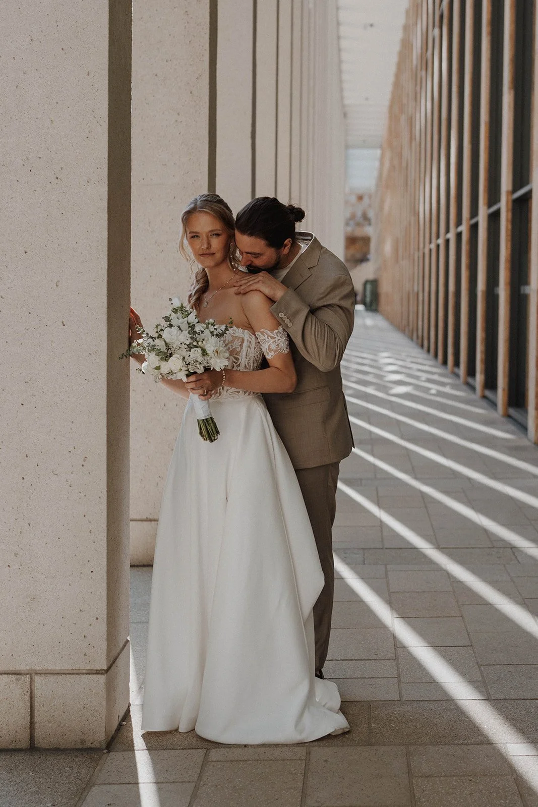 Ein Brautpaar steht nebeneinander, die Braut hält einen Blumenstrauß, der Bräutigam umarmt die Braut und küsst sie auf die Schulter – festgehalten vom Bart van Westrop, Hochzeitsfotograf in Mainz