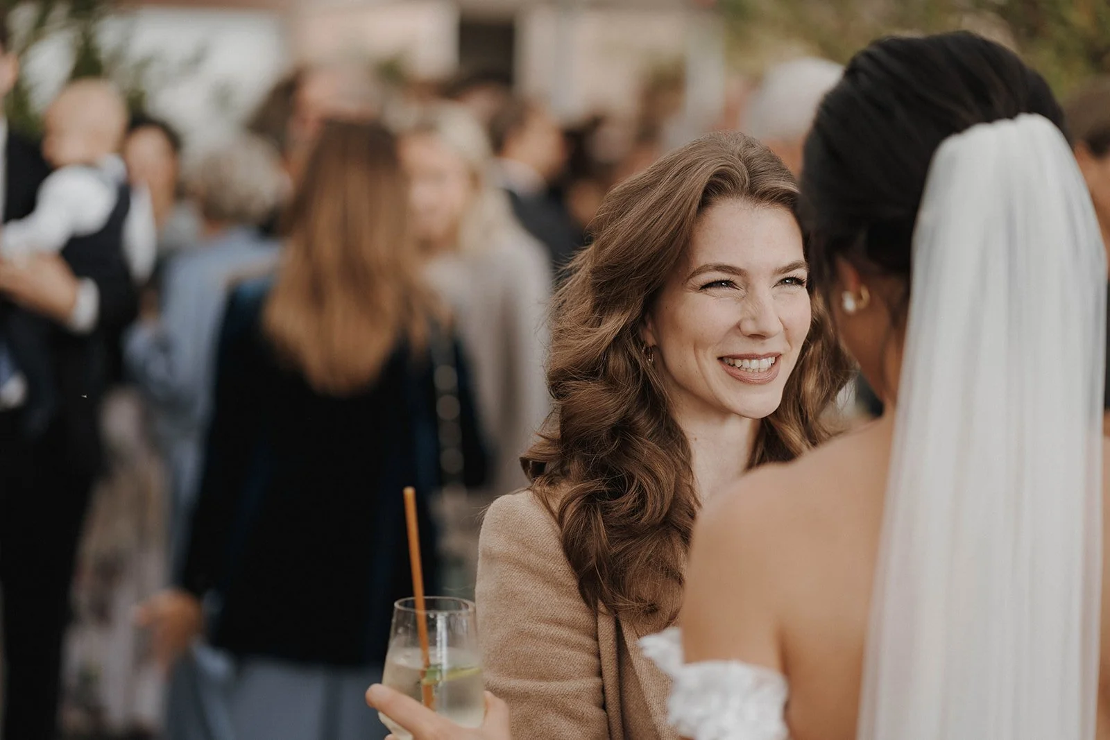 Zwei Frauen, eine ist die Braut während einer Hochzeit, im Hintergrund weitere Gäste – festgehalten vom Bart van Westrop, Hochzeitsfotograf in Mainz