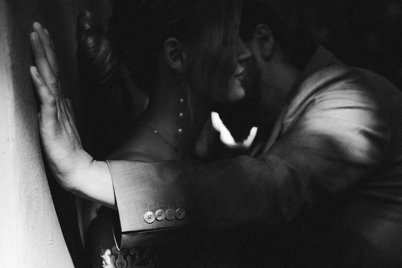 Ein Mann und eine Frau küssen sich in einem dunklen Raum, die Frau lehnt mit dem Rücken an der Wand, beide lächeln – festgehalten vom Bart van Westrop, Hochzeitsfotograf in Mainz